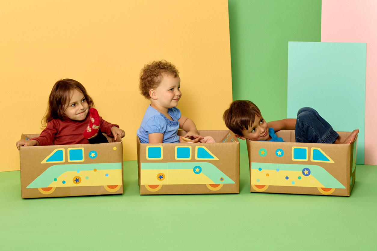 Foto: Drei Kinder sind in Kartons wo Zug und Wagon aufgezeichnet sind