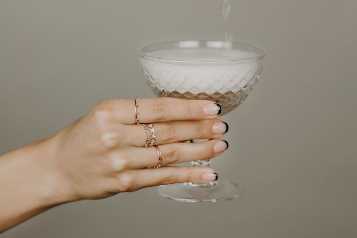 Eine Frauenhand mit Ringen hält ein Champagnerglas mit Champagner.