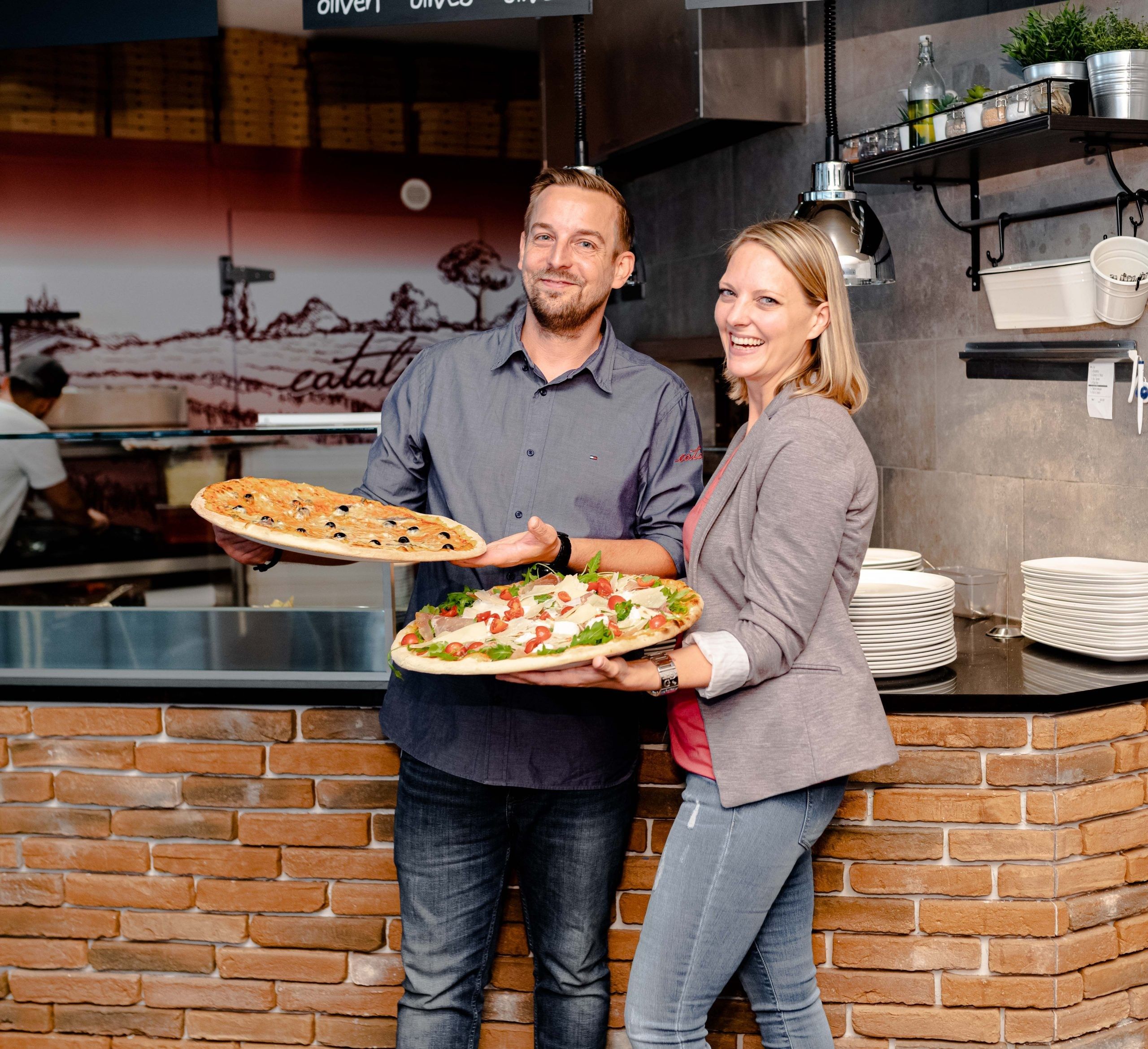 Zwei Personen mit frischen Pizzen in den Händen