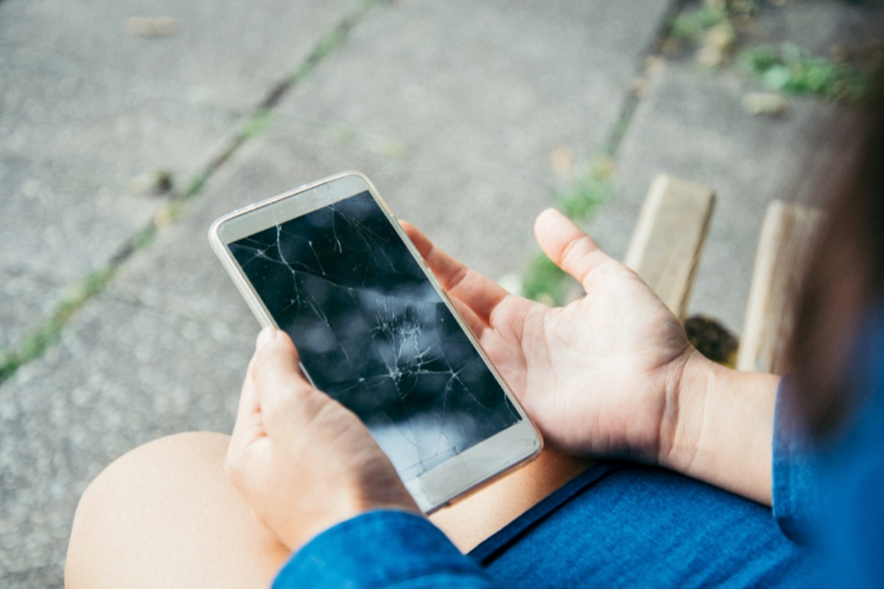 Eine Frau hält ein Handy mit kaputtem Display in der Hand