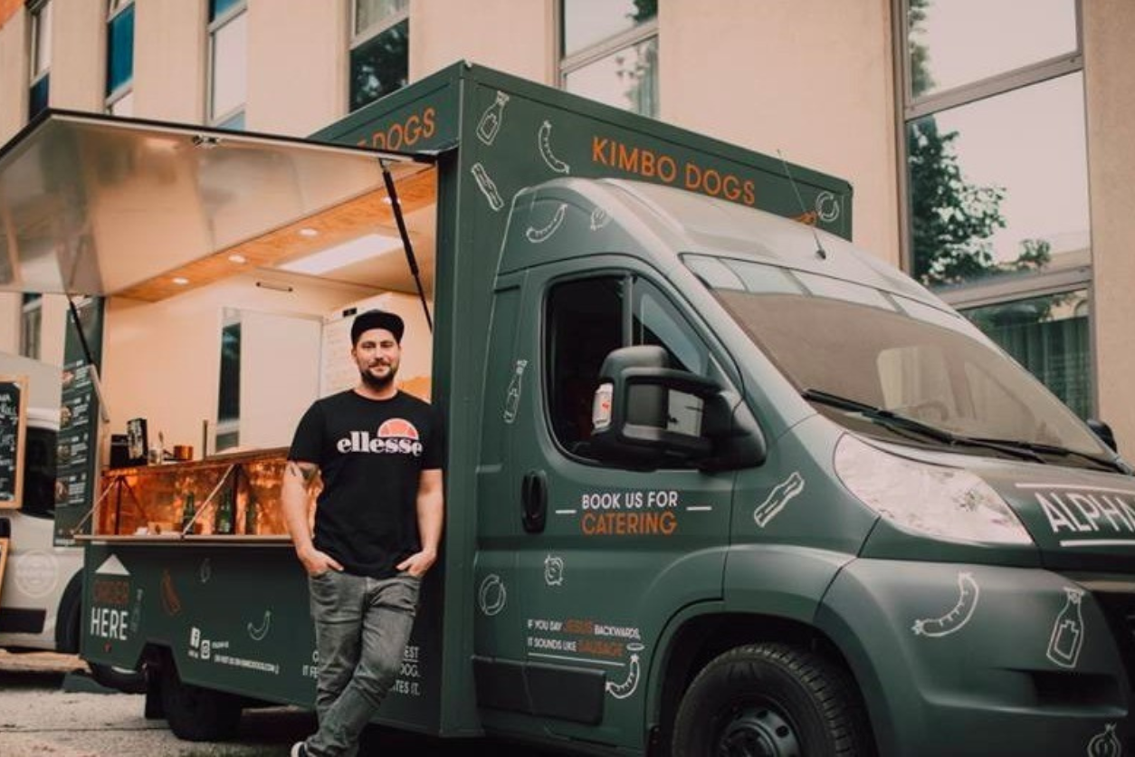 Foodtruck mit geöffneter Seite und einem Mann am LKW angelehnt. 