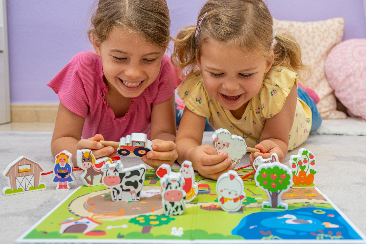 Foto: Zwei Kinder liegen am Boden und spielen mit Spielzeug Tieren