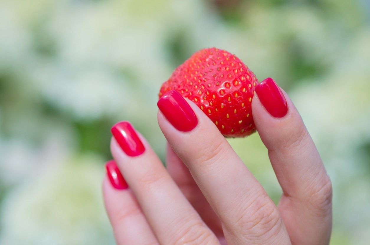 Eine Frauenhand mit roten Fingernägel und einer roten Erdbeere.