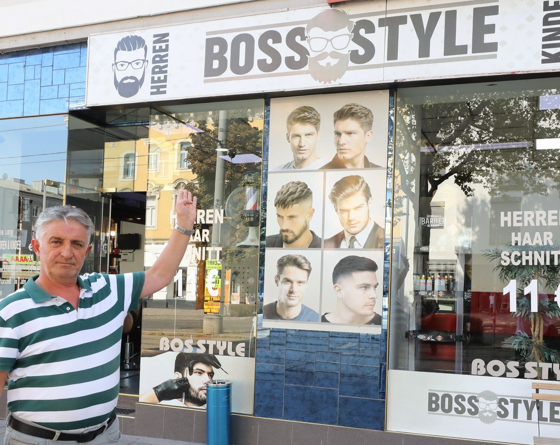 Eingangsbereich von Boss Style, ein Mann zeigt auf die Auslage auf der verschiedene Haarschnitt-Model-Bilder zu sehen sind.