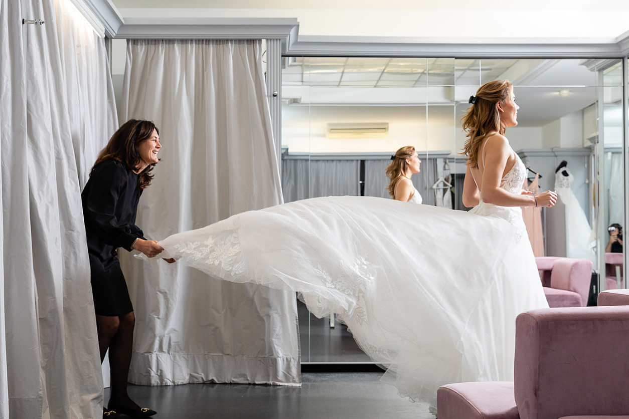 Foto: Eine Frau hat ein Brautkleid an und eine andere hebt das Kleid