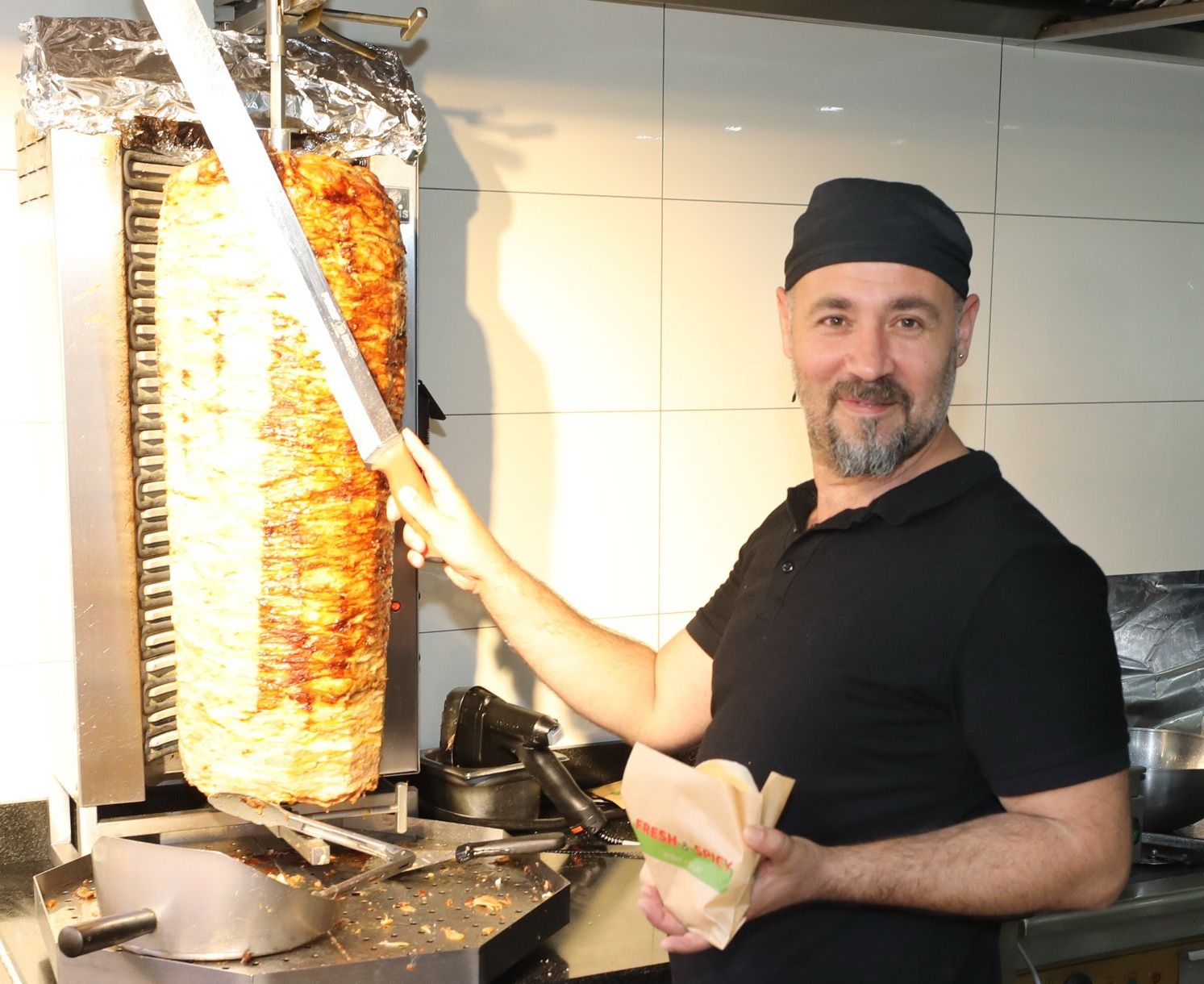 Mann vor Kebap-Spieß der gerade einen Kebap vorbereitet