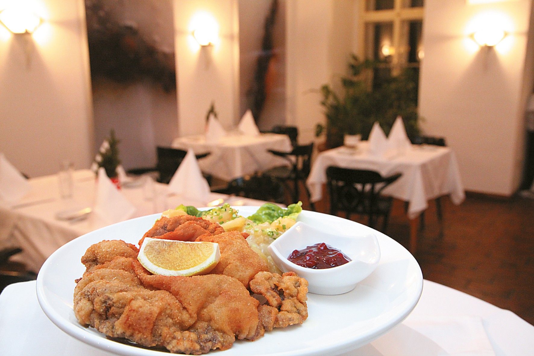 Schnitzel mit Petersilkartoffeln, Preiselbeersoße und Zitrone auf einem Teller platziert