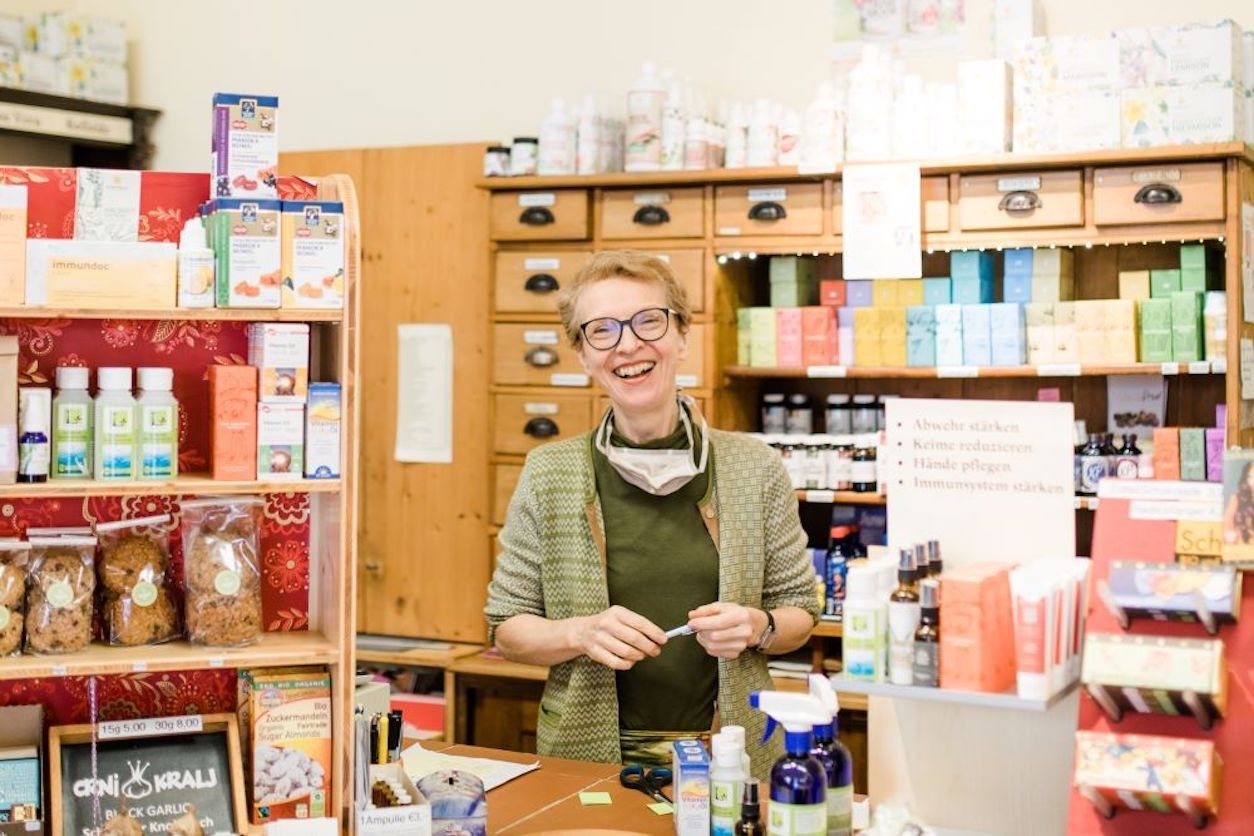 Geschäftsfläche mit Regalen und vielen Produkten. Eine Frau steht hinter dem Tresen. 