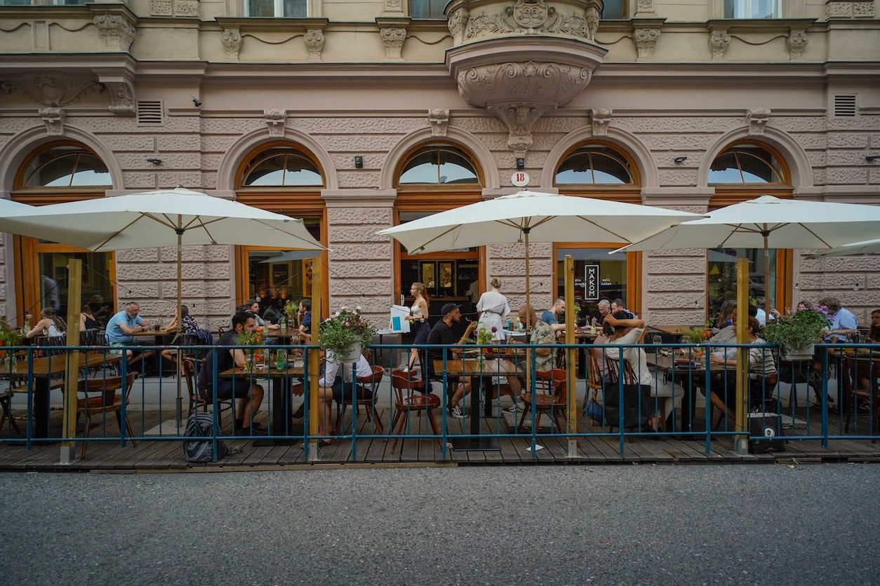 Außenfläche mit Tischen, Stühlen und Schirmen. Viele Personen sitzen.