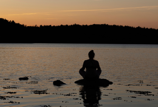 Eine Person sitzt auf einem Stein im Wasser und meditiert